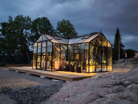 A house being built on a hillside with a trailer. Drivhus Larvik XL 623x381x250cm
