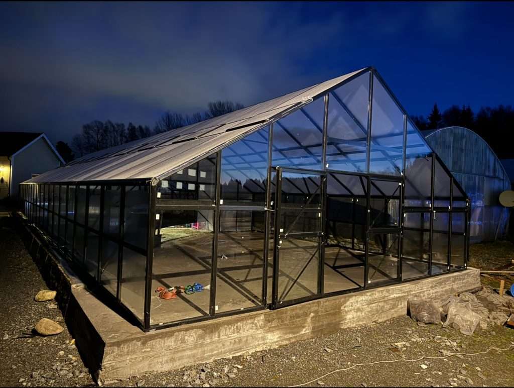 A large greenhouse with a large window at night. Drivhus Tromsø 141,6 m2