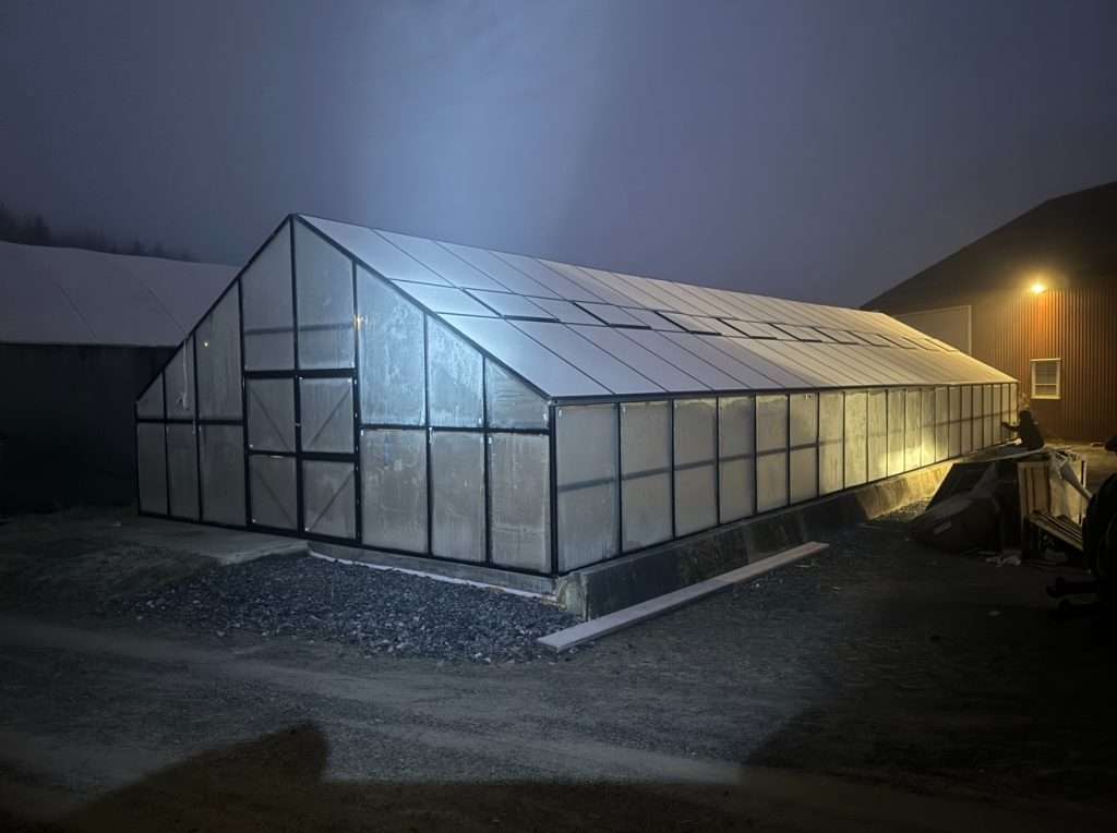 A greenhouse is lit up at night with a light shining on it. Drivhus Tromsø 170 m2