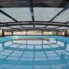 A swimming pool under a roof with a glass wall.